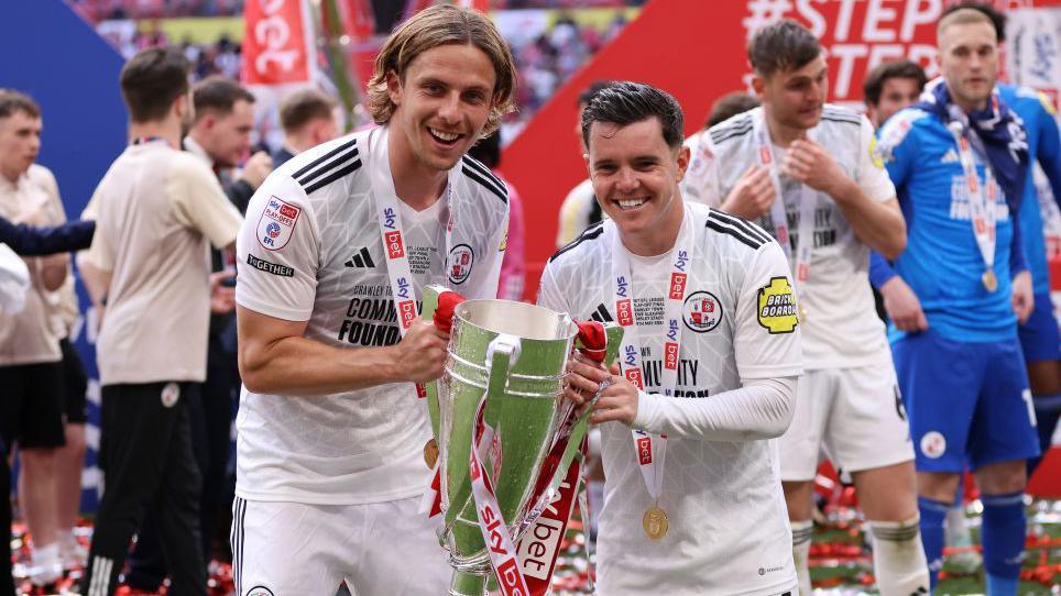 Danilo Orsi and Liam Kelly hold the League Two play-off trophy