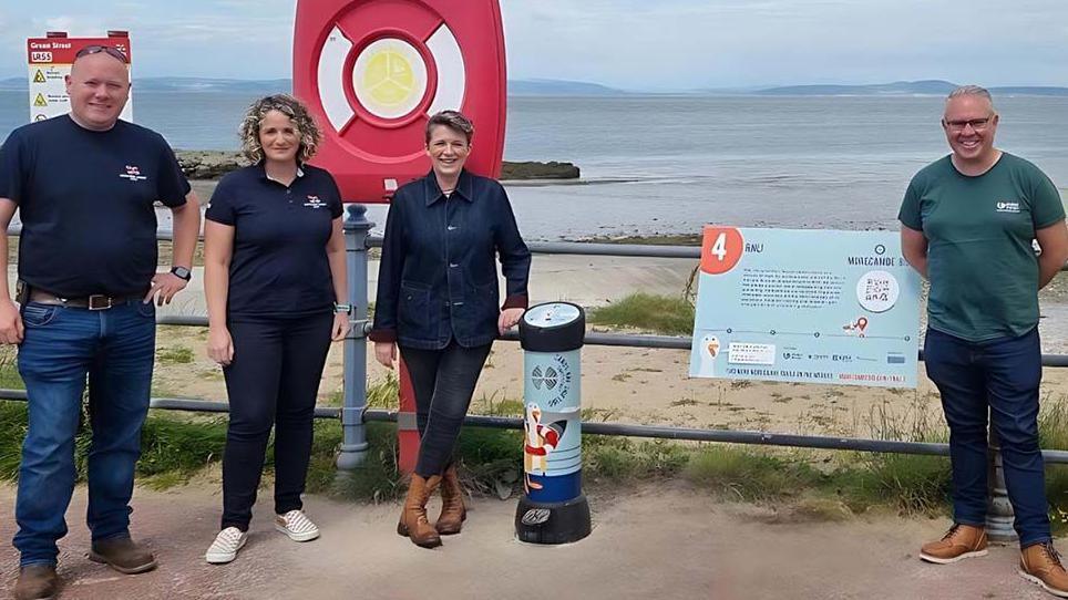 Four people on the promenade standing next to one of the interactive, pedal-powered devices