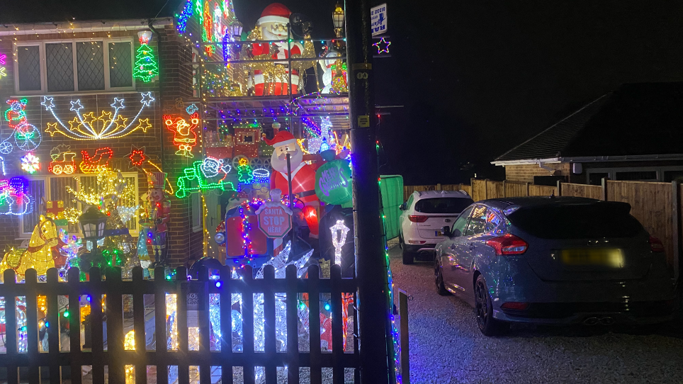 Bright Christmas lights are lit up on a house, with two cars parked next to the property