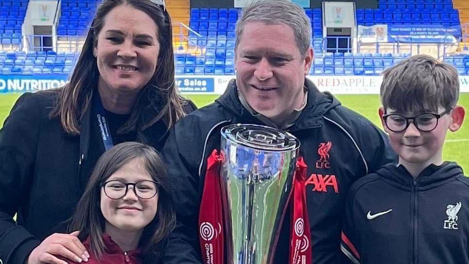 A photograph of Liverpool Women manager Matt Beard celebrating the Championship trophy win with his family