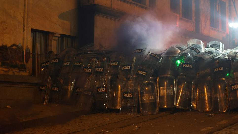 Riot police officers wait in a side street next to parliament as tens of thousands of people protest a short distance away