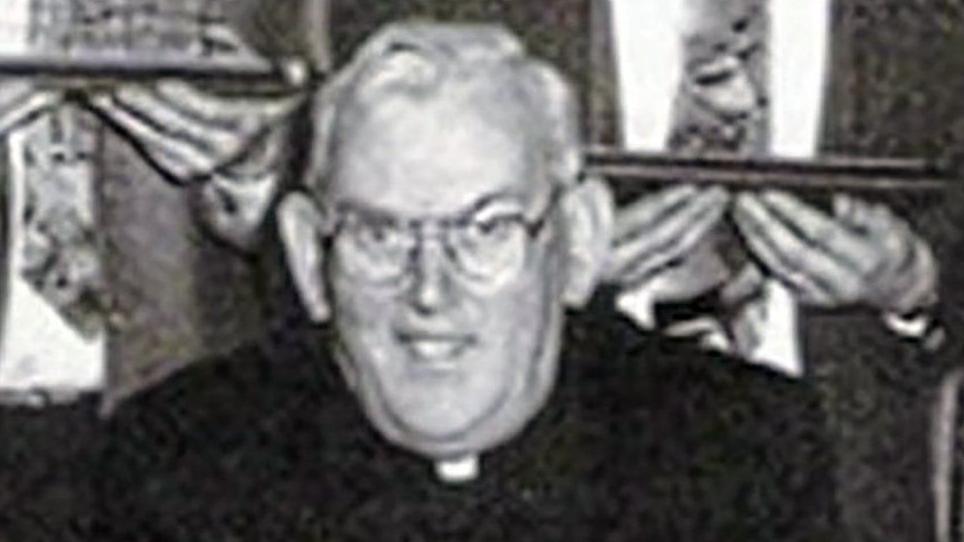 A black and white photo of the late Fr Malachy Finegan.  He is wearing glasses, a black suit and a priest's collar.