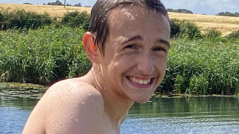 Alfie Brown, pictured with him having been swimming in a river. Behind him are reeds on the far side of the river.