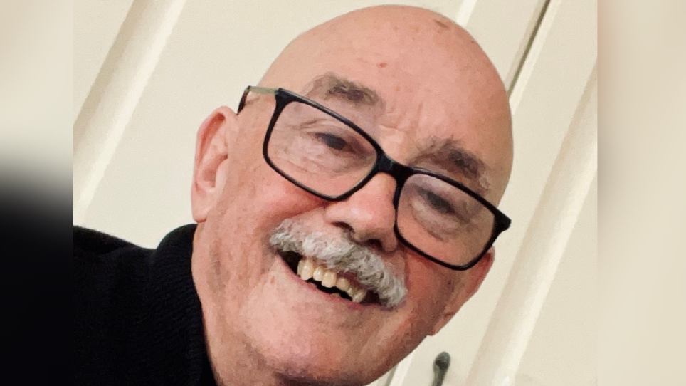 Thomas Noel Crowley pictured smiling at the camera. He has a grey moustache, is bald and wears black rimmed glasses and a black top.