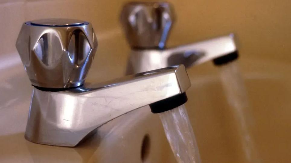 A close up of two silver taps with clear water pouring out of them into a sink.