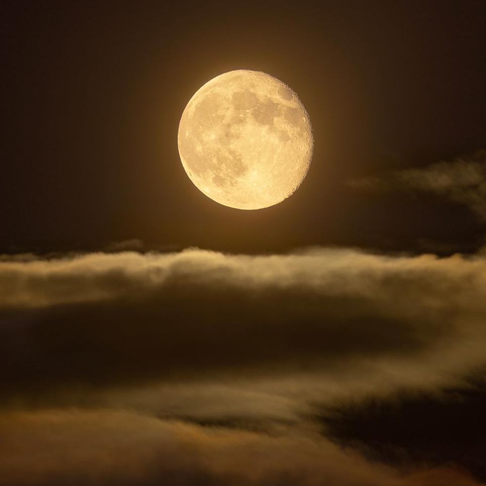 The full moon above clouds has a yellow glint to it