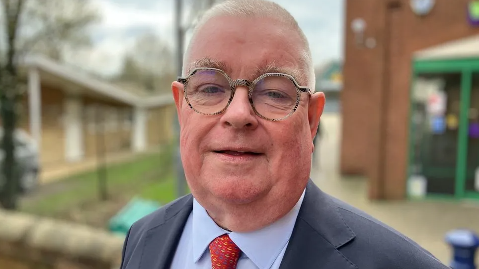 John Tizard smiling for camera in a blue suit and red tie 