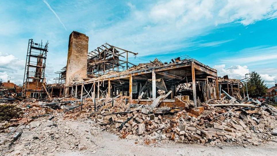 Rubble surrounds the charred remnants of a building with blue sky in the background