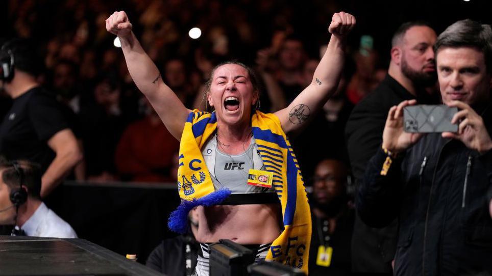 Molly McCann celebrates at cageside with an Everton scarf 