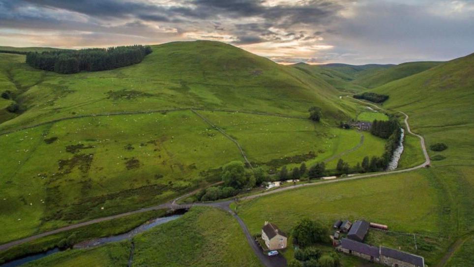 An aerial view of Barrowburn in Upper Coquetdale a remote valley in Northumberland. The landscape is green with a farm in the foreground and a river winding down through a steep sided valley 