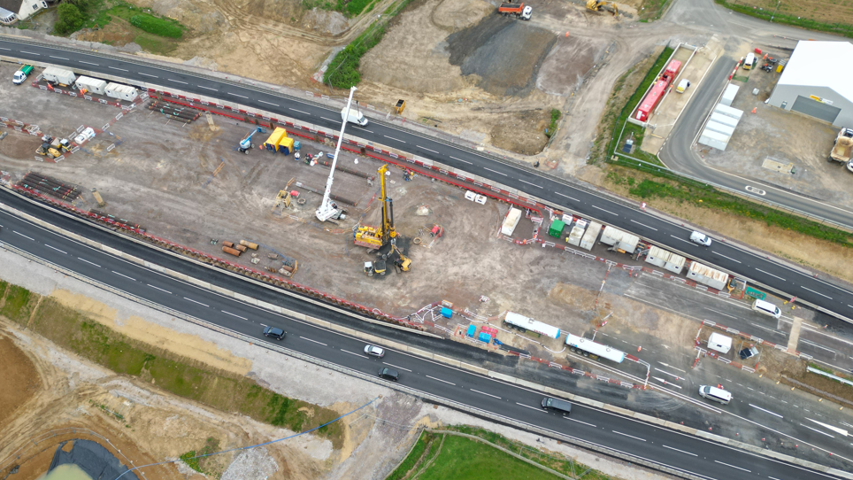 An aerial view of a construction site with cranes over a dual carriageway.