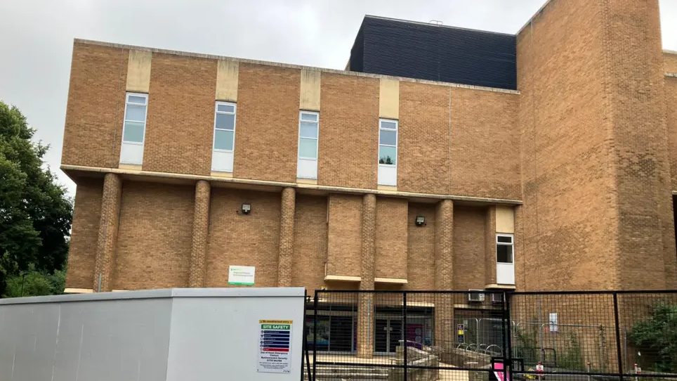 Exterior of the Regional Pool- brown brick building with  black fencing in front 