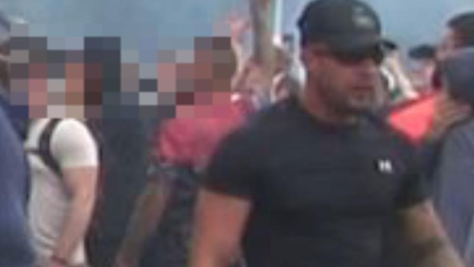 Police image of a man with a black baseball cap, black t-shirt and some blurrier images of people behind him