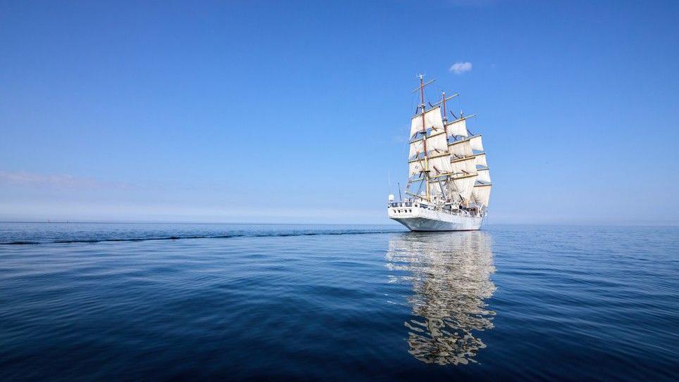 The vessel sailing off towards the horizon on a dark blue sea with bright blue sky above.