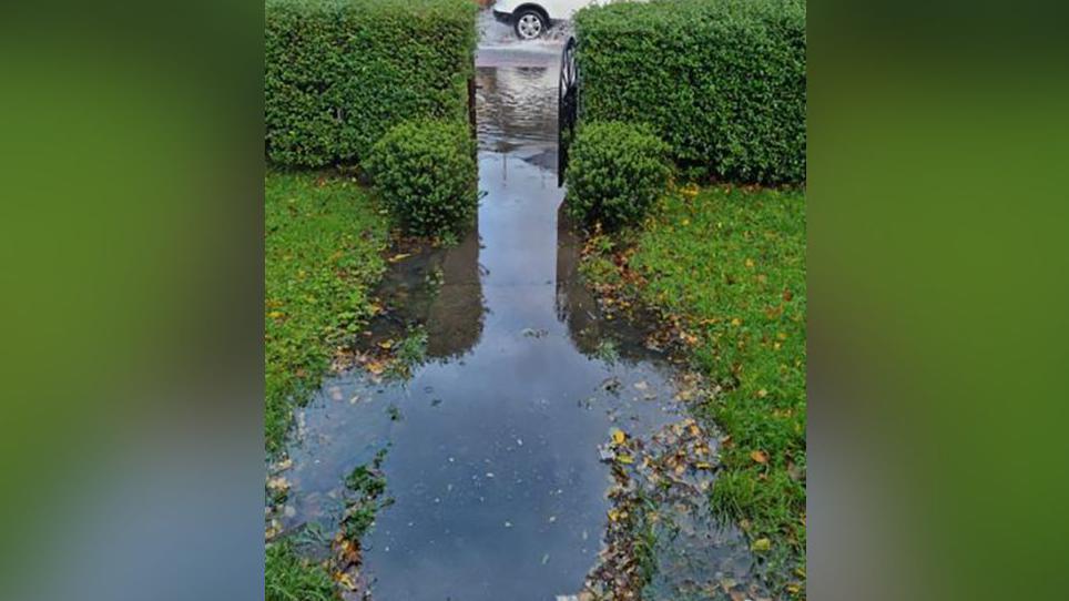 Garden path and the road flooded with water. A white car is seen driving through surface water on the road in 2023. 