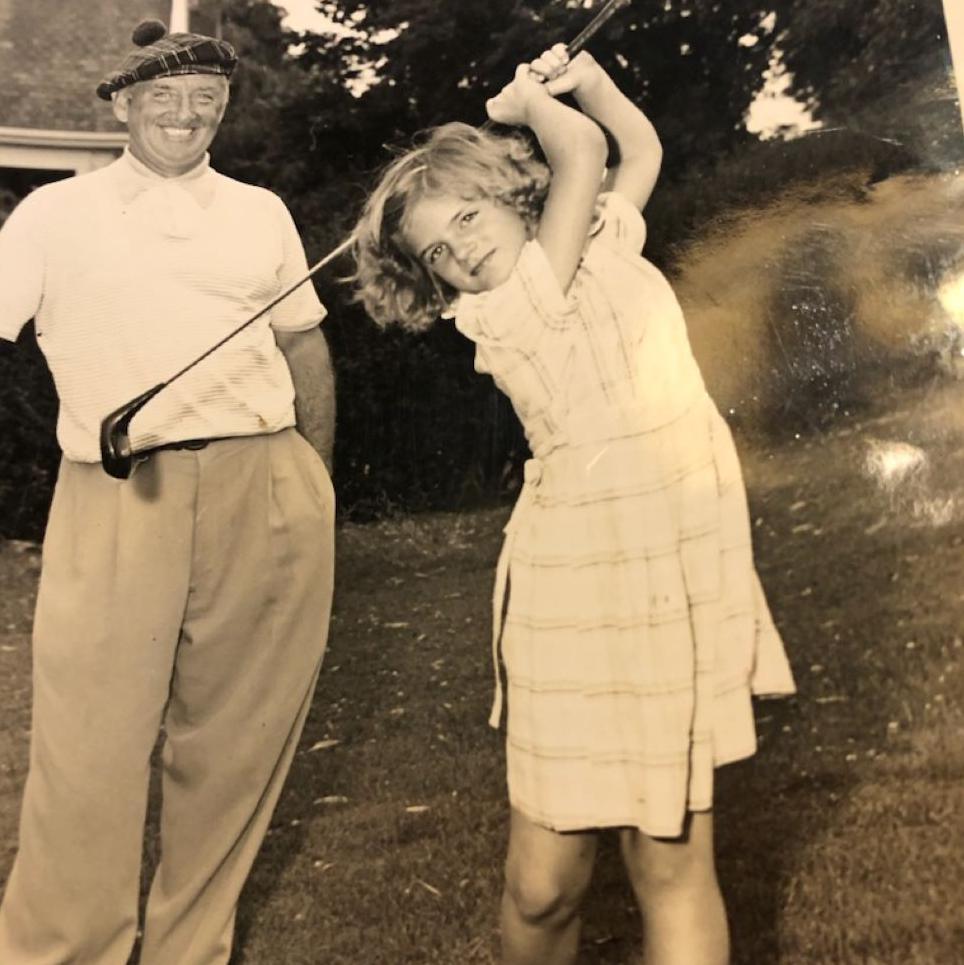 Sepia image of young girl, Diana Smith, in a dress swinging a golf club, with her grandfather Bobby Cruickshank smiling and looking on.