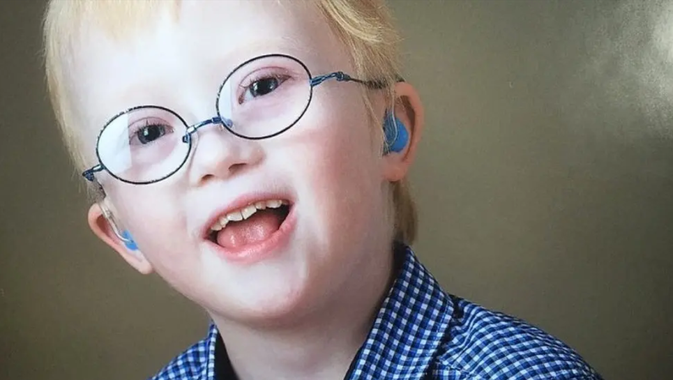A portrait picture of James Dwerryhouse. He has blond hair and is wearing glasses with a round frame. His mouth is open and he is looking at the camera. He is wearing a blue chequered shirt.