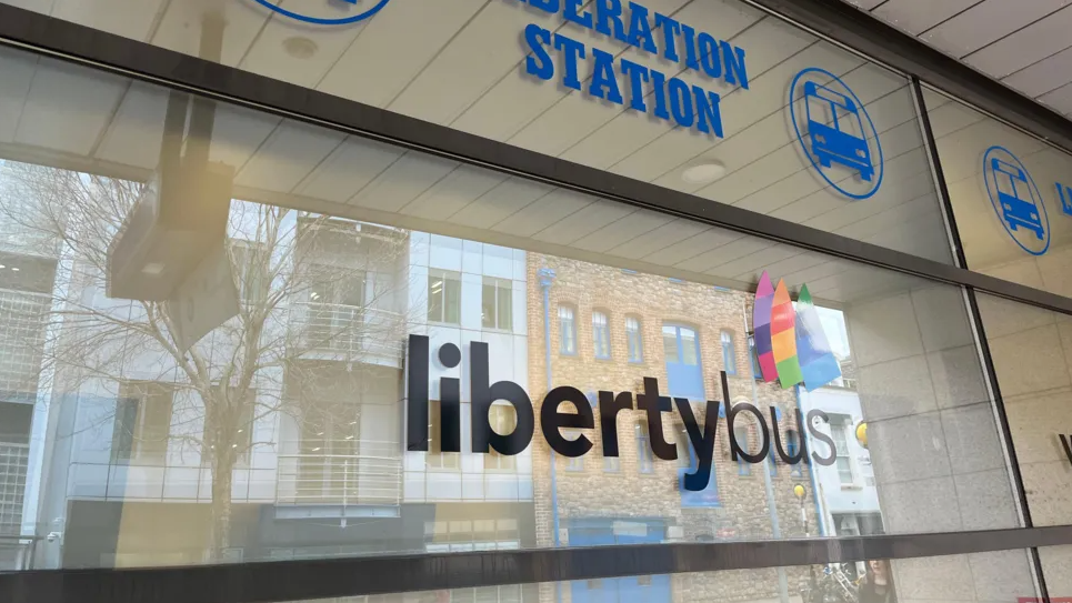 Glass private tinted wall with black libertybus sign in the middle, dark blue sign above saying LIBERATION STATION and a bus emoji in a circle in dark blue