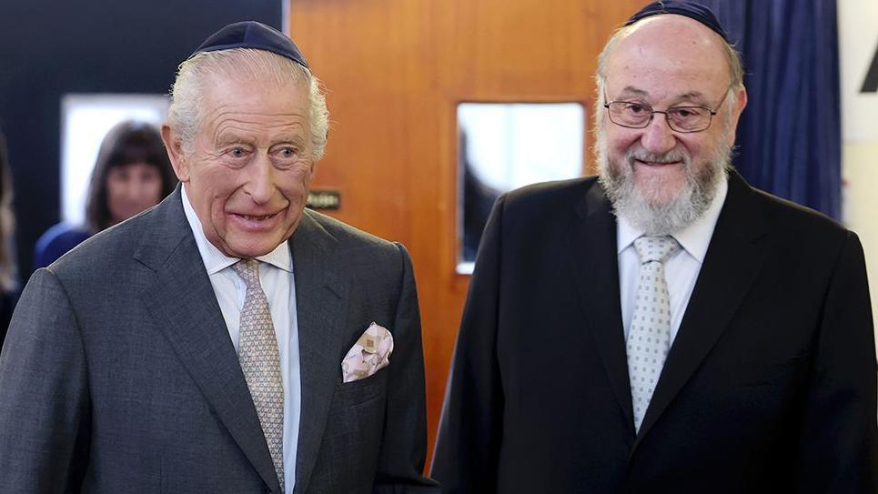 King Charles (left) wears a kippah and grey suit as he stands with Chief Rabbi Sir Ephraim Mirvis during his visit to Heaton Park Hebrew Congregation Synagogue.