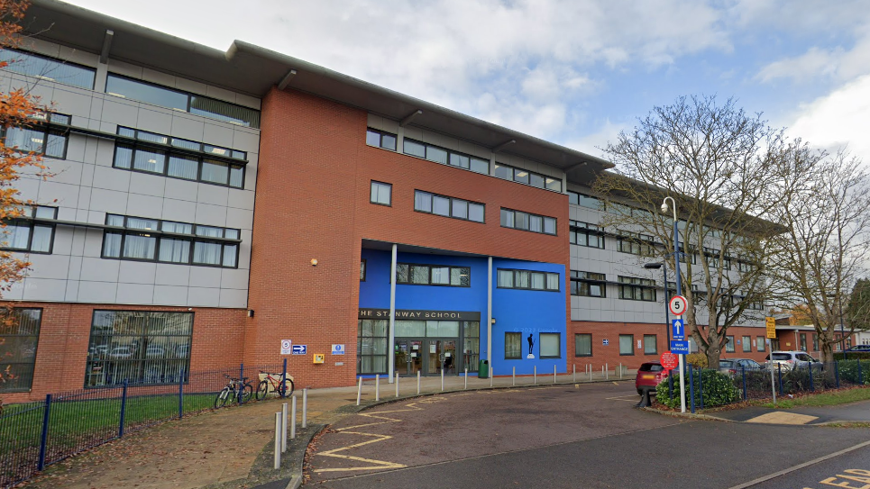 The entrance to The Stanway School. It is a large building which is grey, orange and blue in appearance.