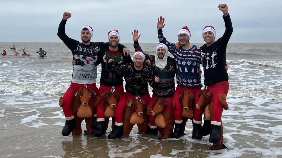 Six men dressed in Christmas jumpers and in reindeer fancy dress outfits in the sea