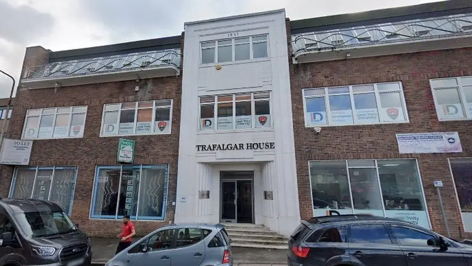 The building has a white front section with its name above the door and some steps leading to the entrance with windows either side.