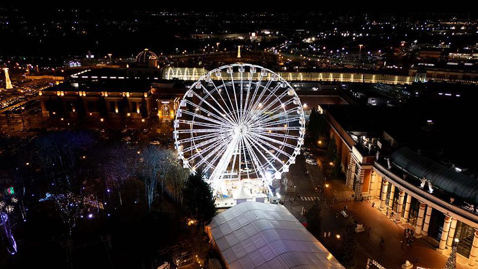Aerial view of the Trafford Centre at night showing the big wheel light up in white lights as part of the fairground.