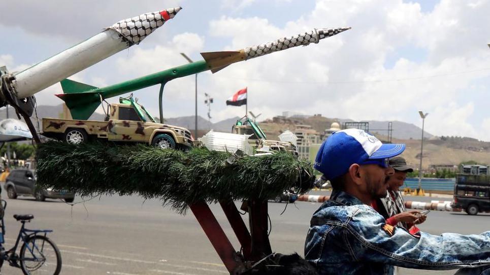 Houthi militiaman rides in front of sculpture of missiles