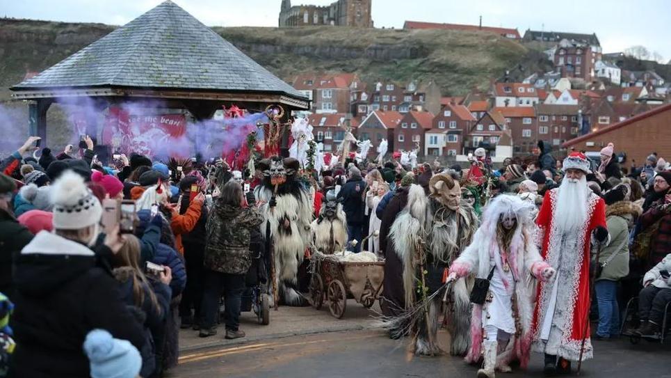 A crowd of people gather in Whitby for Whitby Krampus Run in 2023. Many are dressed up as Krampus, which is a half goat half demon figure with horns. 