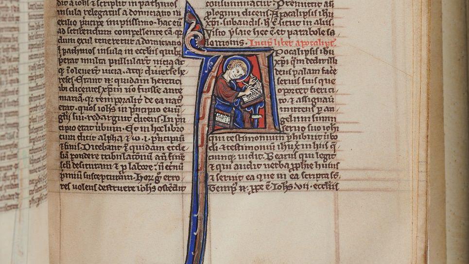 An old manuscript page, in tiny, perfectly written medieval Latin. One starting letter to a Bible book - an A - is lavishly decorated in blue and red and shows a monk with pen and knife writing sitting inside the letter. The A tails off dramatically, like a branch or root.