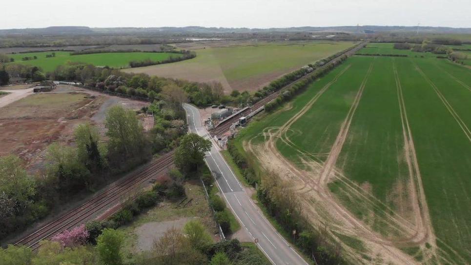 An aerial view of fields surrounding a junction between a road and railway track