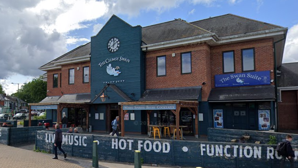 The exterior of the Clumsy Swan pub in Birmingham, a red brick building with dark blue wooden entrance and hoarding around an outdoor drinking area.