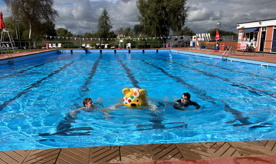 Two men swimming in a lido outdoor pool with Pudsey bear 