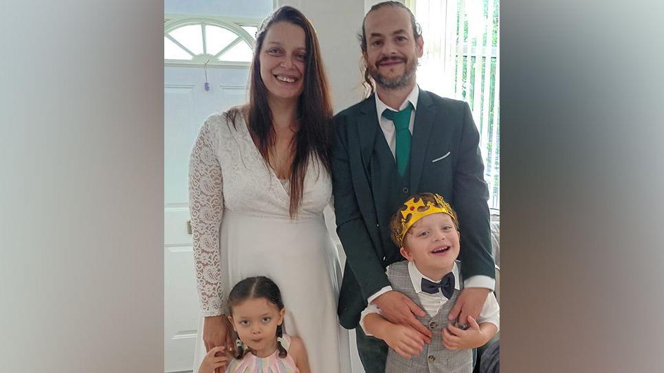 David Wrag and his wife Sara are pictured in a family photo with their children by their sides, dressed in smart clothes and the son wearing a paper crown on his head