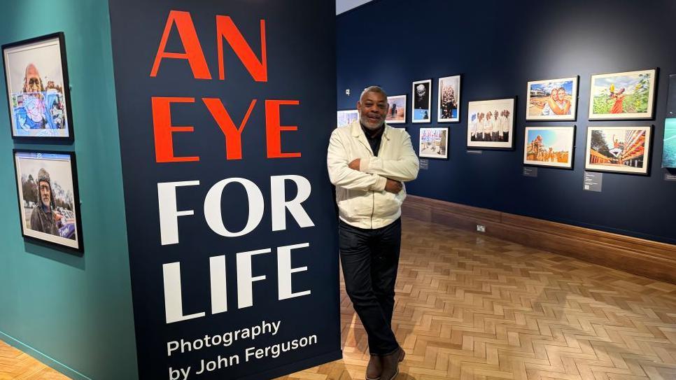 John Ferguson standing in the exhibition space at Christchurch Mansion surrounded by his photographs on the walls.