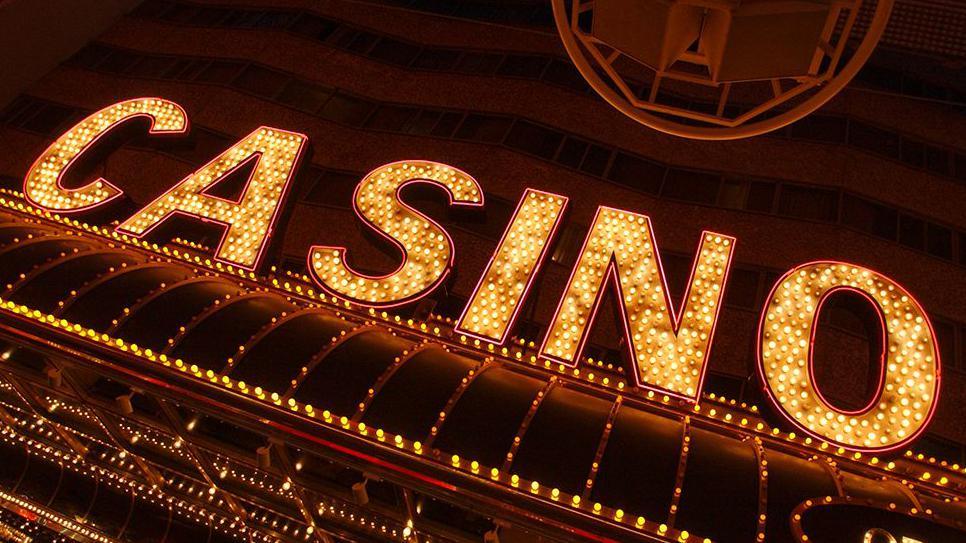 A sign against a dark background that says casino in capital letters made up of small yellow light bulbs. The sign is angled slightly to the bottom left corner