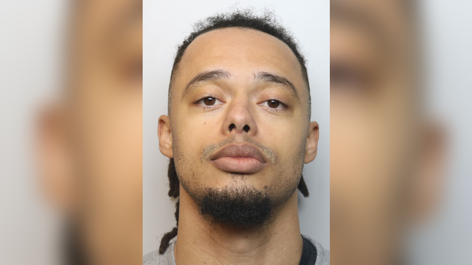 Tre Mitford looking at the camera in a police mugshot. He has a goatee and has his head angled up a little so that it looks like he's looking down at the camera.