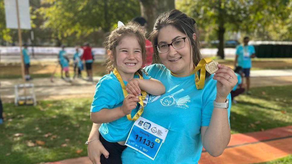 Ruby and mum Danielle are smiling at the camera. They are both wearing blue T-shirts and are holding race medals. 