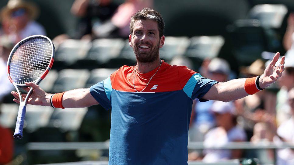 Cameron Norrie, in blue and orange shirt, celebrates his victory against Alex de Minaur by smiling and stretching both arms out by his side