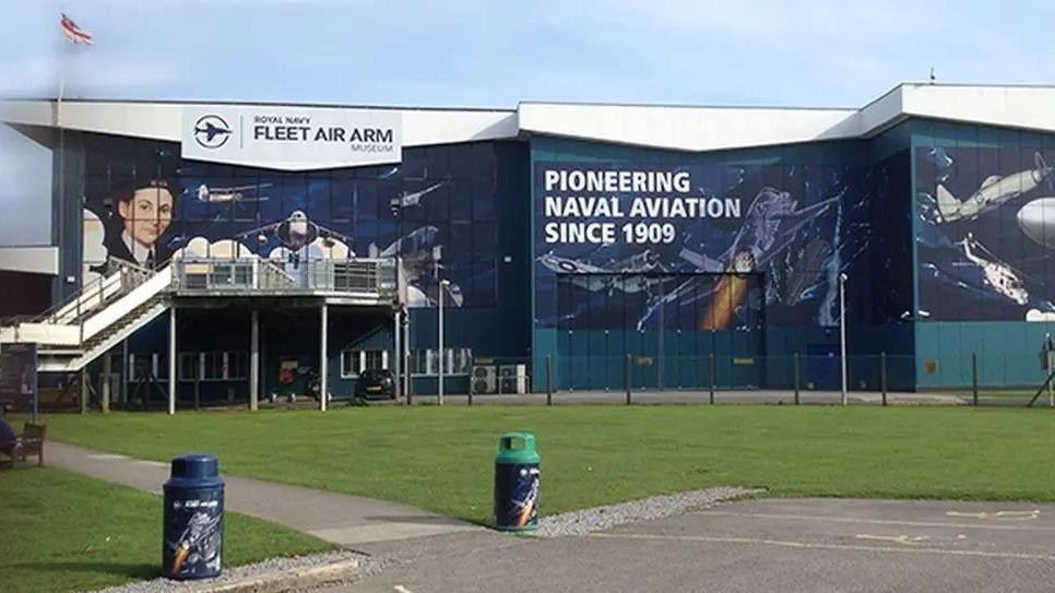 External shots of the Fleet Air Arm Museum, which is mostly navy and says "Pioneering Naval Aviation Since 1909" on the building.