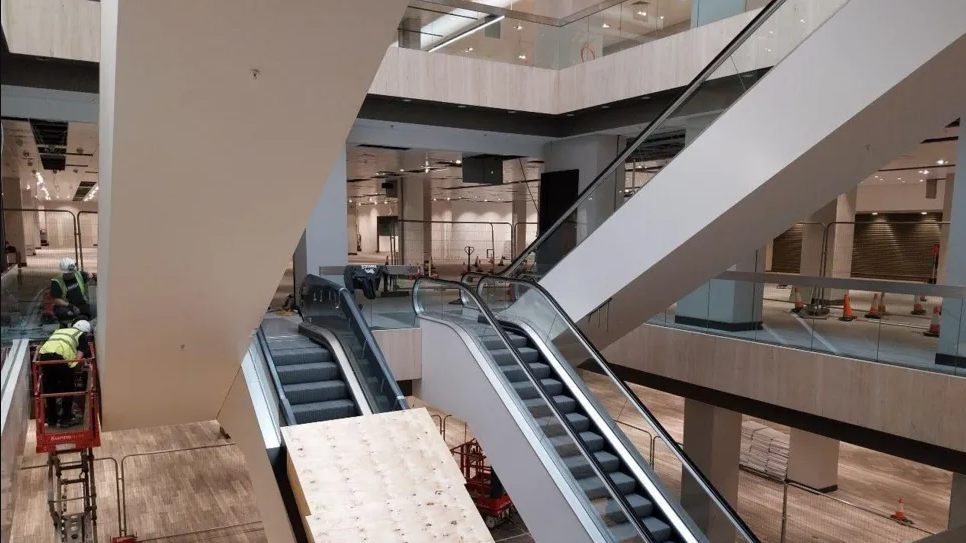 An under construction unit with two sets of escalators and workmen wearing high visibility jackets 