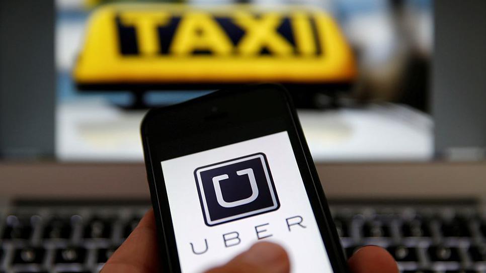 An illustration picture shows the logo of car-sharing service app Uber on a smartphone next to a picture of a taxi sign