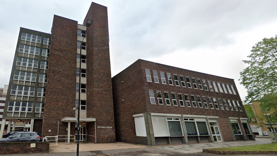 A seven-storey building to the left of the picture and a wider three -storey building to the right of that making part of Upton Lodge. They are made from brown and red brick with lots of small rectangular windows and a sign saying, "Upton Lodge" on the taller building next to an entranceway 