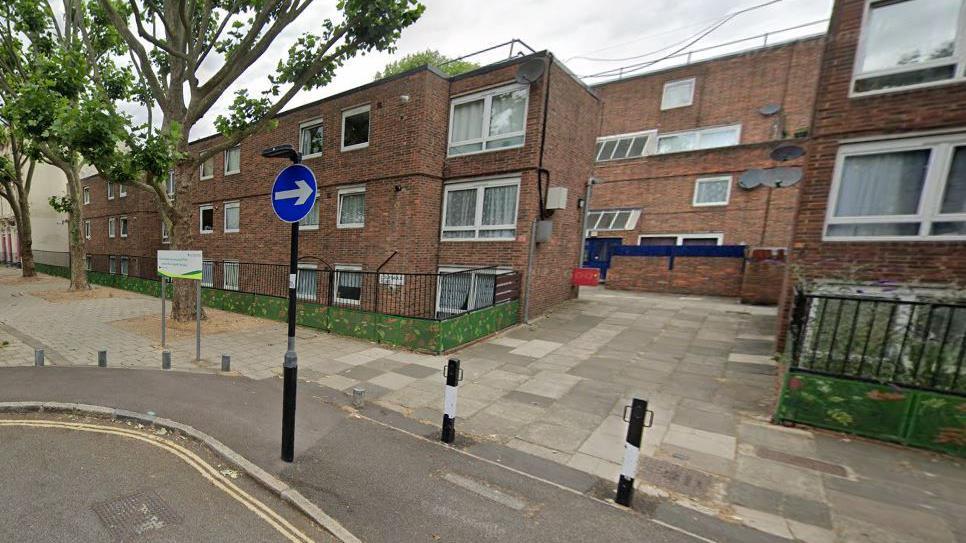 A Street View image showing Courtauld Road, on the corner of Beachcroft Way, with a small lamppost and two bollards in front of small blocks of flats