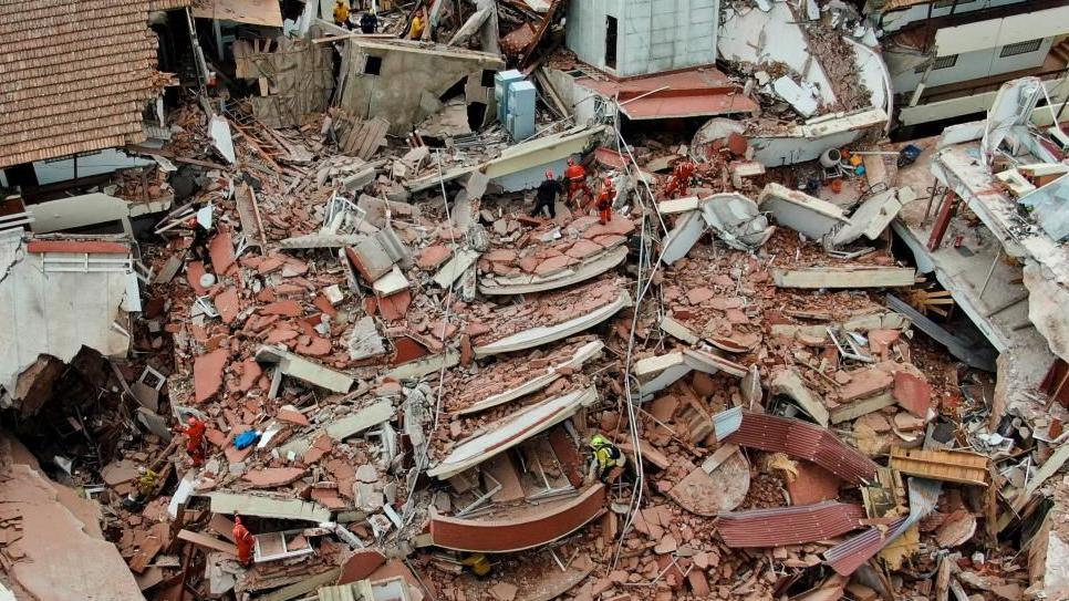 Aerial drone photograph shows the widespread debris and damage from the hotel collapse from a bird's eye view. Rescue workers can be seen scaling the debris with a range of apparatus and emergency workwear. 