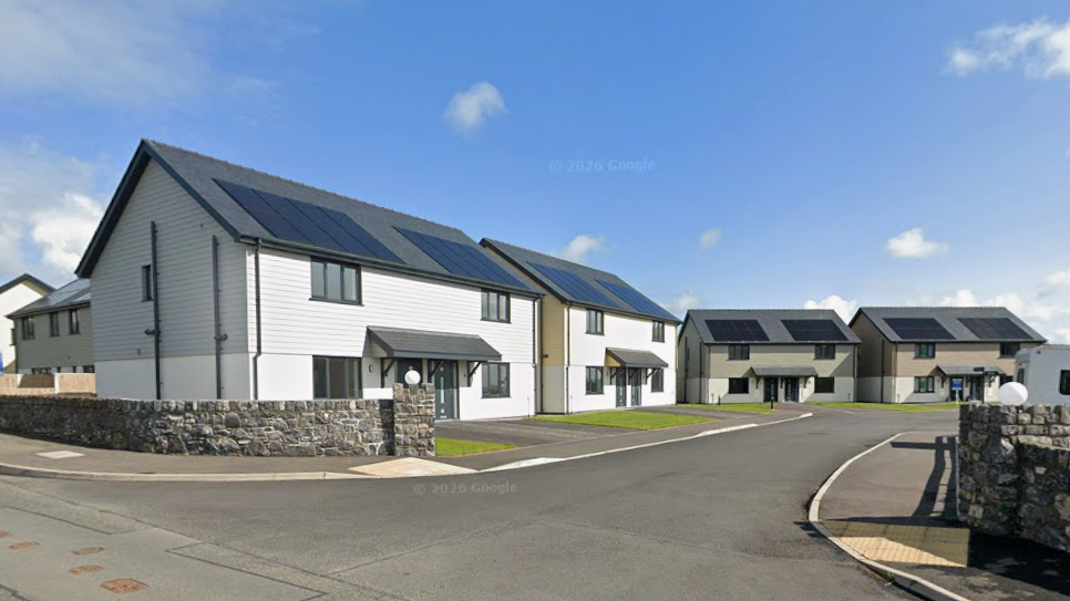 A cul-de-sac of semi-detached modern homes lining a road. They all have solar panels on the roof with wooden cladding on the top of the buildings, and each has a grey porch roof. 
