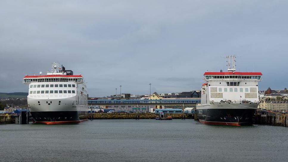 Two large white, black and red ferries sit close to each other in the sea at Douglas Harbour.