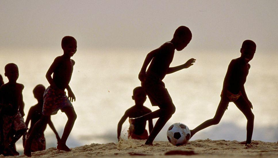 Boys in silhouette playing football on a beach in Ghana.