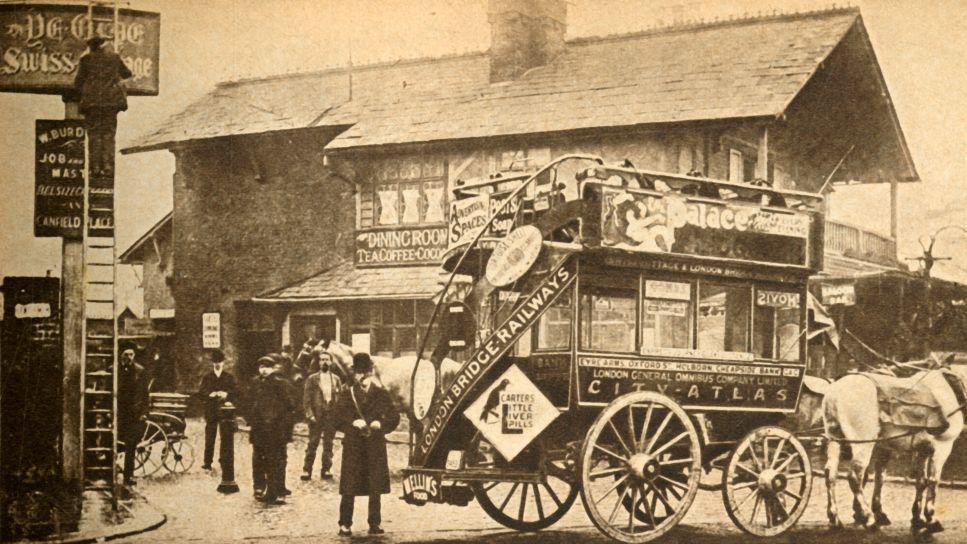 A sepia-toned historic photo of Ye Olde Swiss Cottage pub, with a horse-drawn omnibus in the foreground and Victorian-era pedestrians nearby. The chalet-style building features signage for dining and tea, capturing a lively late 19th or early 20th-century street scene.