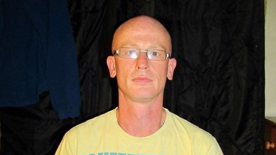 A head-and-shoulders picture of Stuart Caldicott. He has a shaven head and is wearing a yellow t-shirt and glasses.